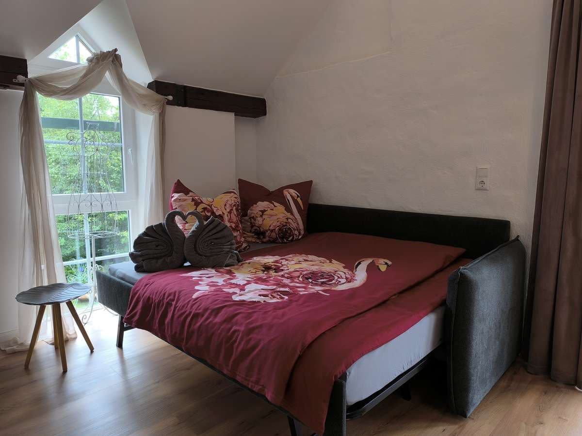 Schlafsofa (160x200cm) mit bordeauxroter Bettwäsche am Giebelfenster im Balkonzimmer